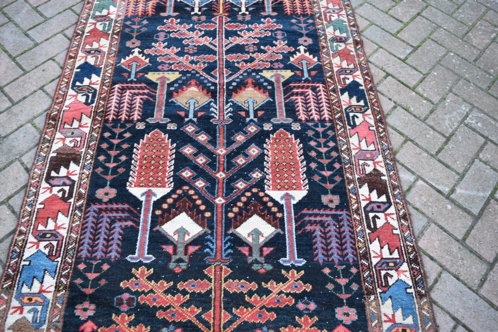 A long antique Persian Bakhtiari runner rug featuring stylised tree motifs in red, blue, and pink on a dark navy ground with a geometric border. View VI