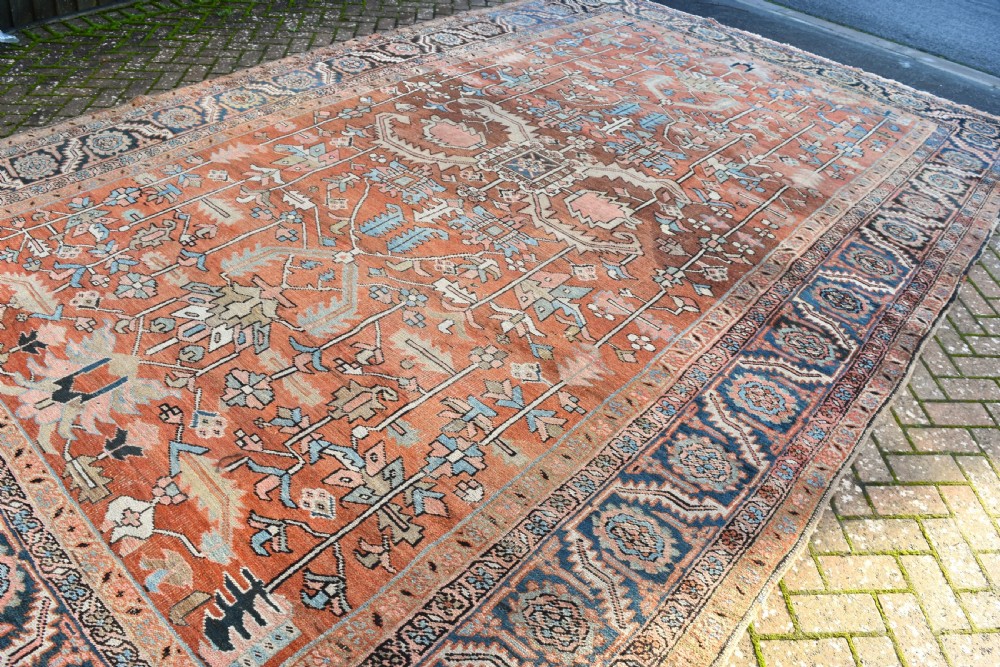 A large hand-knotted Persian Heriz carpet featuring a bold geometric central medallion on a terracotta field with navy blue and cream borders. View III