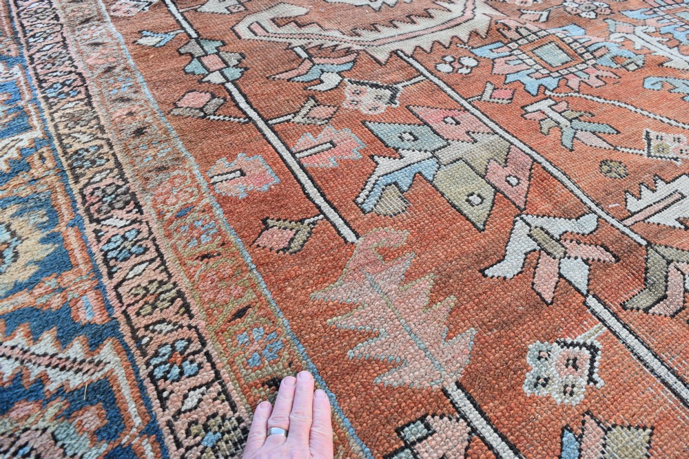 A large hand-knotted Persian Heriz carpet featuring a bold geometric central medallion on a terracotta field with navy blue and cream borders. View IV