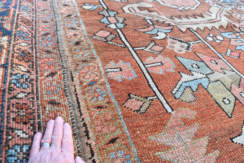 A large hand-knotted Persian Heriz carpet featuring a bold geometric central medallion on a terracotta field with navy blue and cream borders. View V