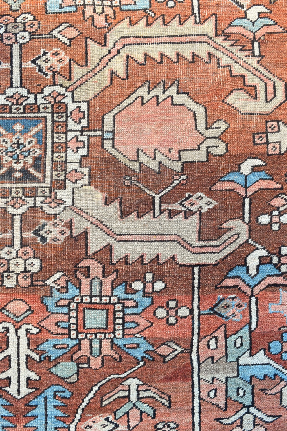 A large hand-knotted Persian Heriz carpet featuring a bold geometric central medallion on a terracotta field with navy blue and cream borders. View VI