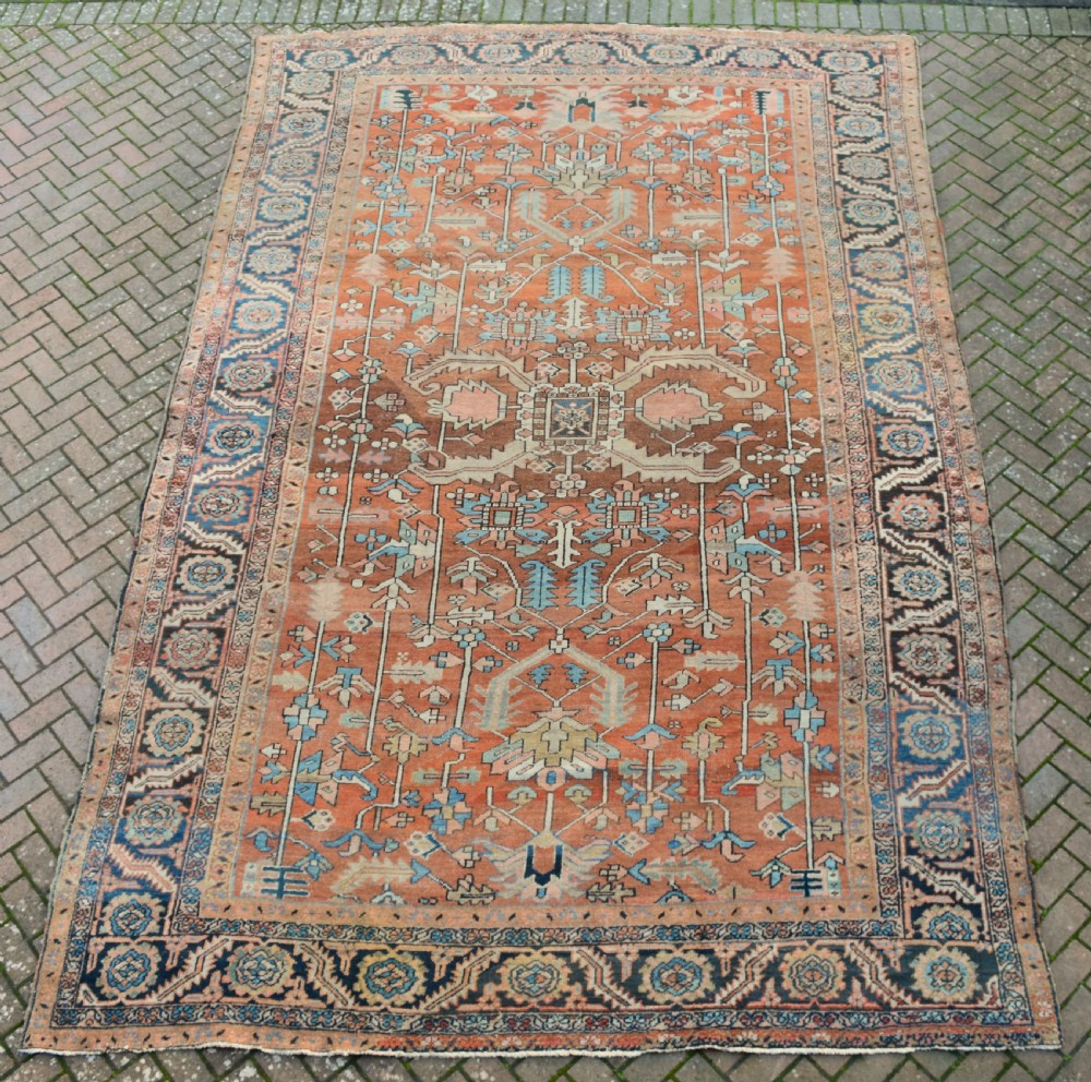 A large hand-knotted Persian Heriz carpet featuring a bold geometric central medallion on a terracotta field with navy blue and cream borders. View VII