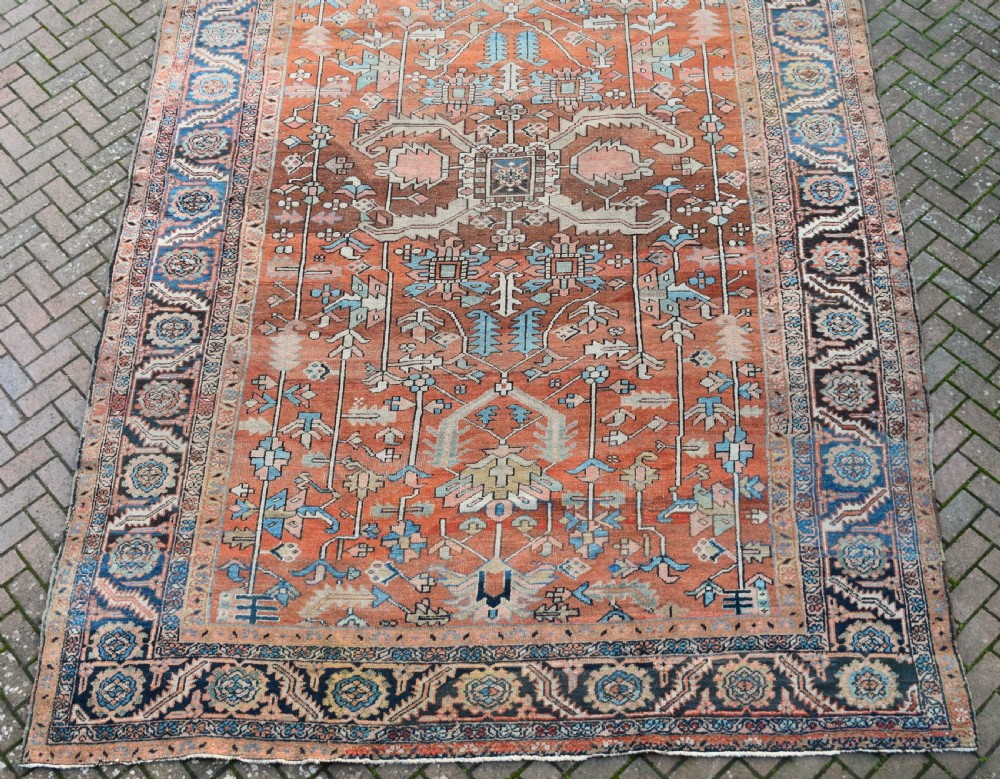 A large hand-knotted Persian Heriz carpet featuring a bold geometric central medallion on a terracotta field with navy blue and cream borders. View VIII