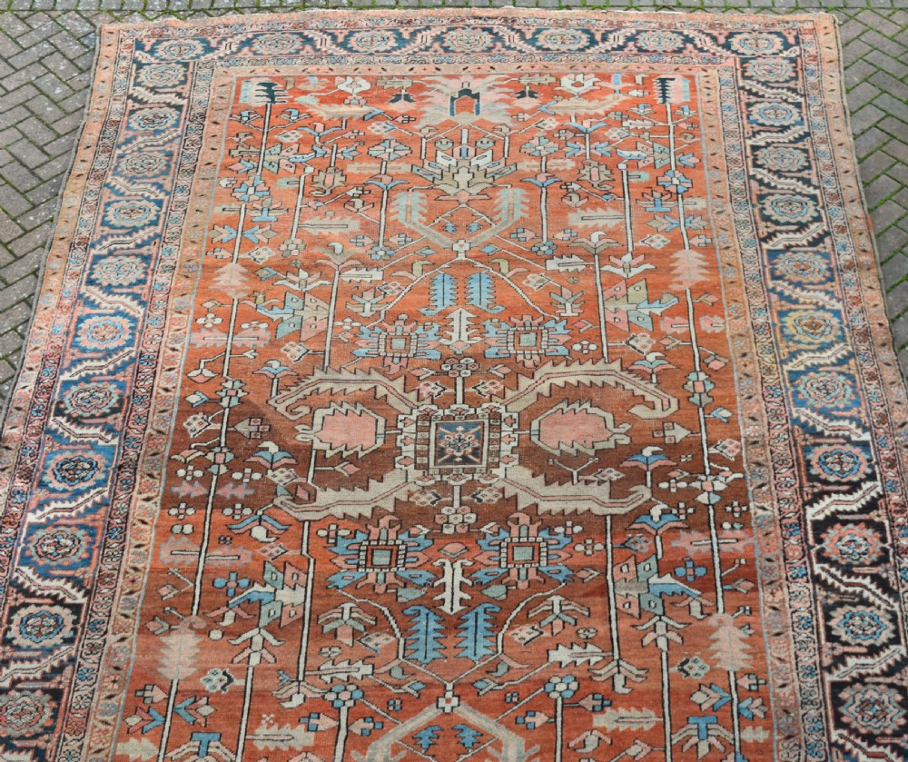 A large hand-knotted Persian Heriz carpet featuring a bold geometric central medallion on a terracotta field with navy blue and cream borders. View IX