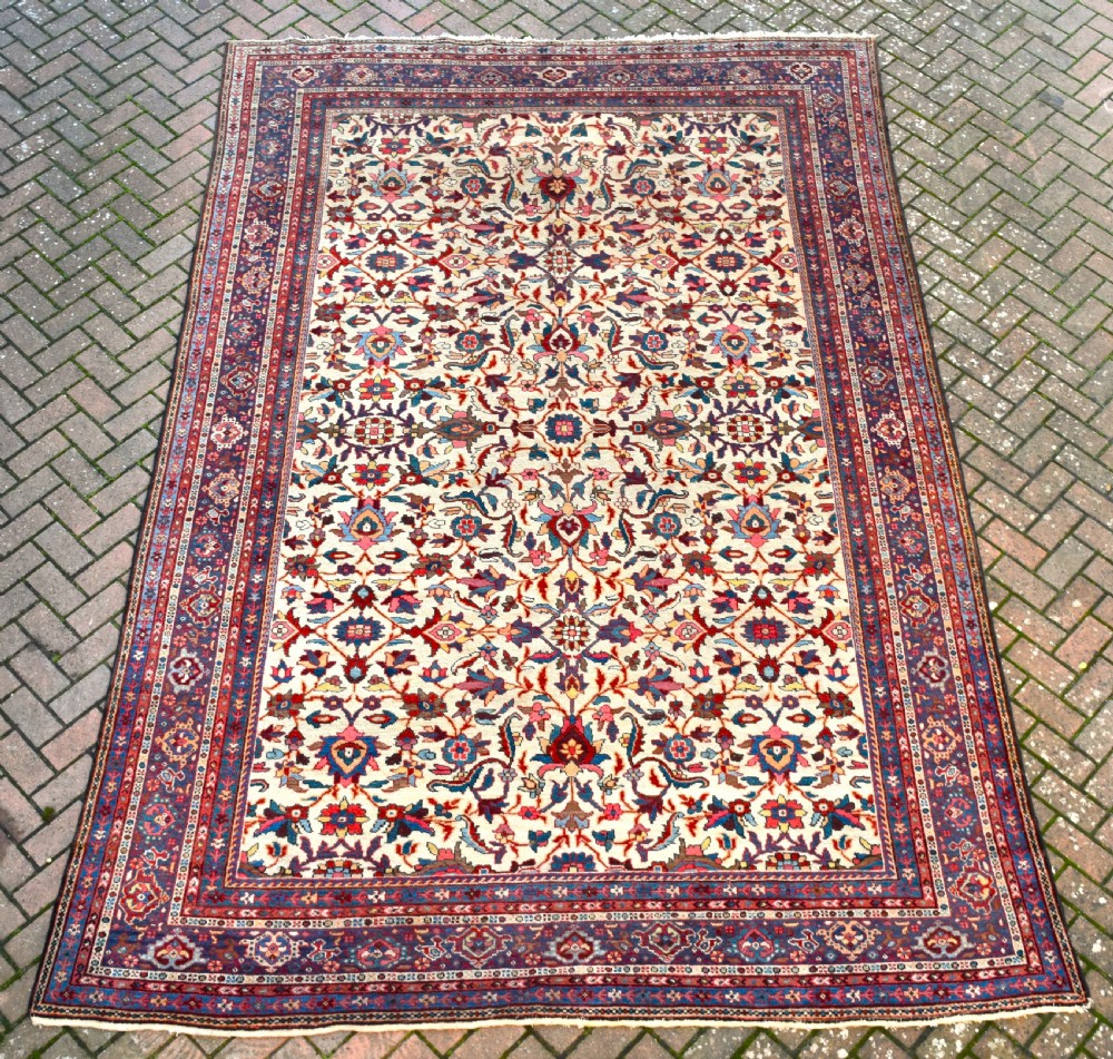 A large hand-knotted Persian Mahal carpet featuring an cream field with red, blue, and terracotta floral palmettes enclosed by a multi-band navy and red border.