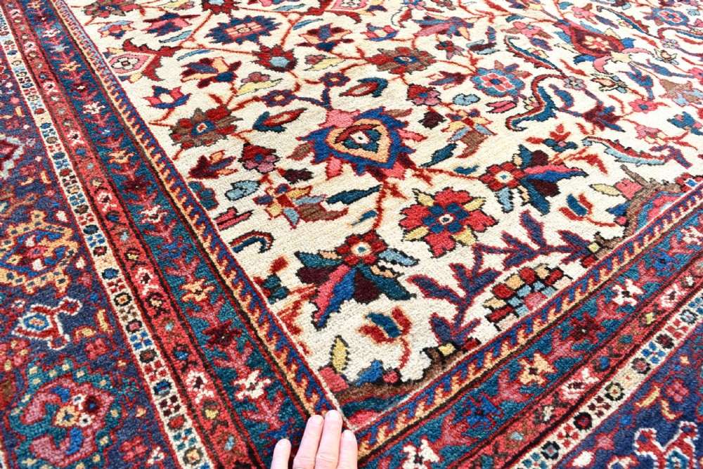 A large hand-knotted Persian Mahal carpet featuring an cream field with red, blue, and terracotta floral palmettes enclosed by a multi-band navy and red border. View V