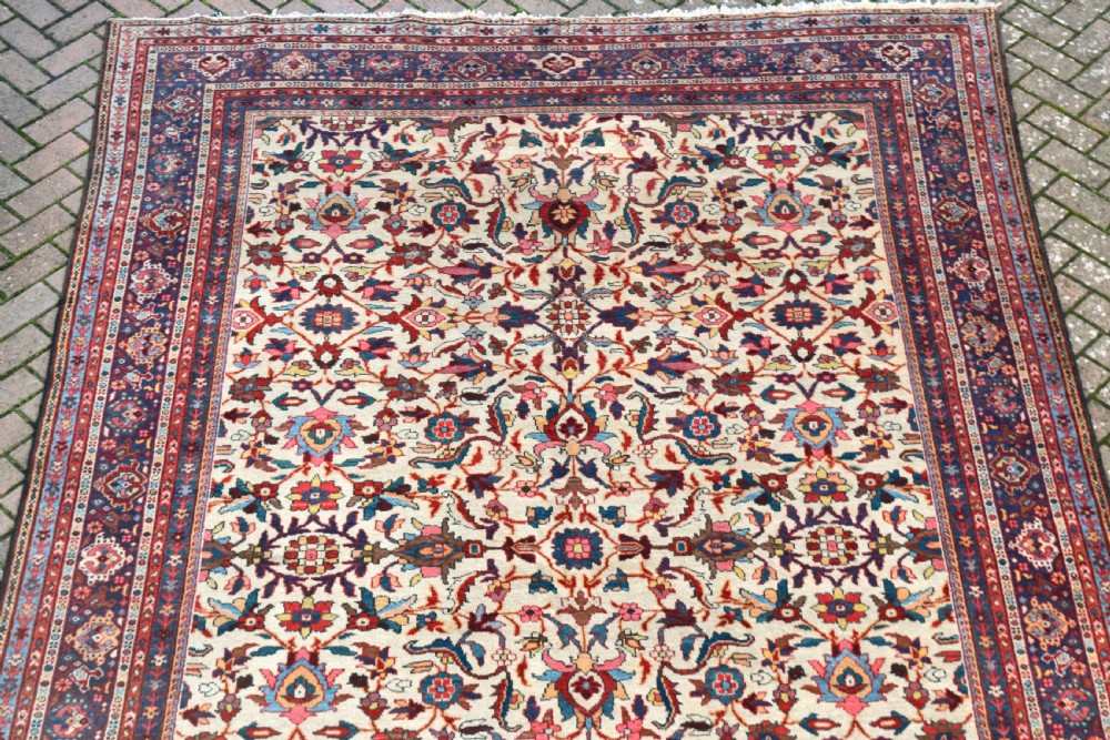 A large hand-knotted Persian Mahal carpet featuring an cream field with red, blue, and terracotta floral palmettes enclosed by a multi-band navy and red border. View VII