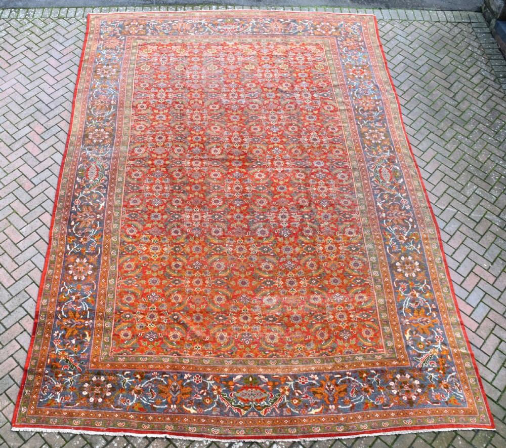 A large rectangular hand-knotted Sultanabad rug featuring an all-over floral lattice pattern on a terracotta red field with a slate blue palmette border.
