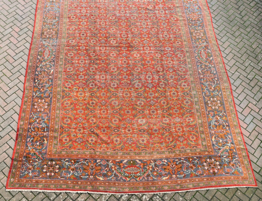 A large rectangular hand-knotted Sultanabad rug featuring an all-over floral lattice pattern on a terracotta red field with a slate blue palmette border. View IX