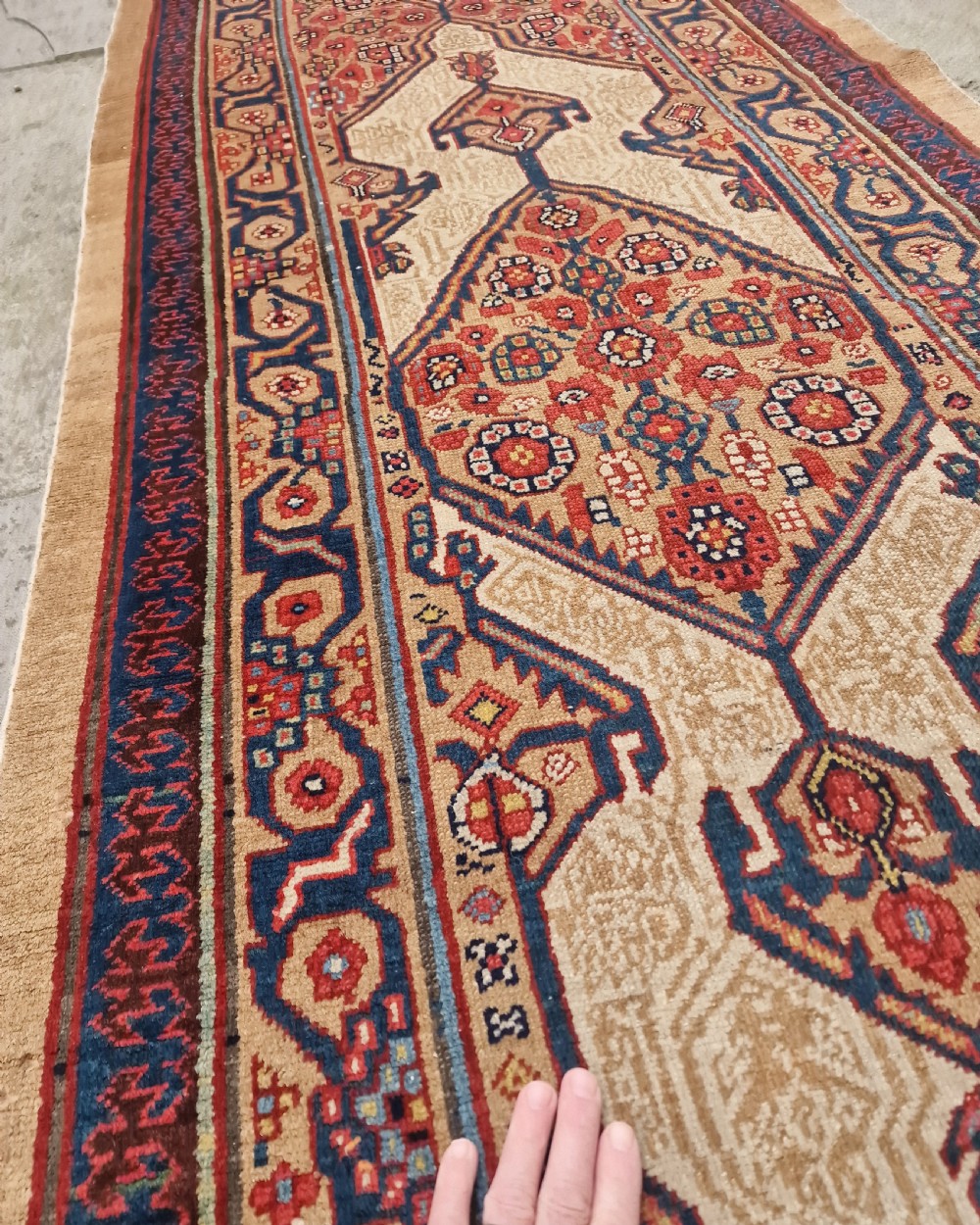 A long, narrow antique Persian Serab wool carpet runner featuring geometric diamond medallions on a camel-coloured field with red and navy patterned borders. View III