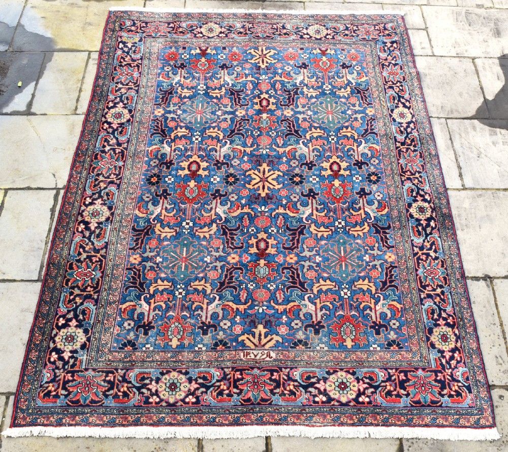 A hand-knotted wool carpet featuring an intricate blue central field covered in geometric floral motifs surrounded by a red and navy patterned border.