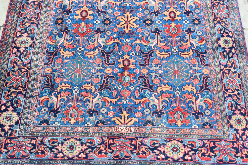 A hand-knotted wool carpet featuring an intricate blue central field covered in geometric floral motifs surrounded by a red and navy patterned border. View II