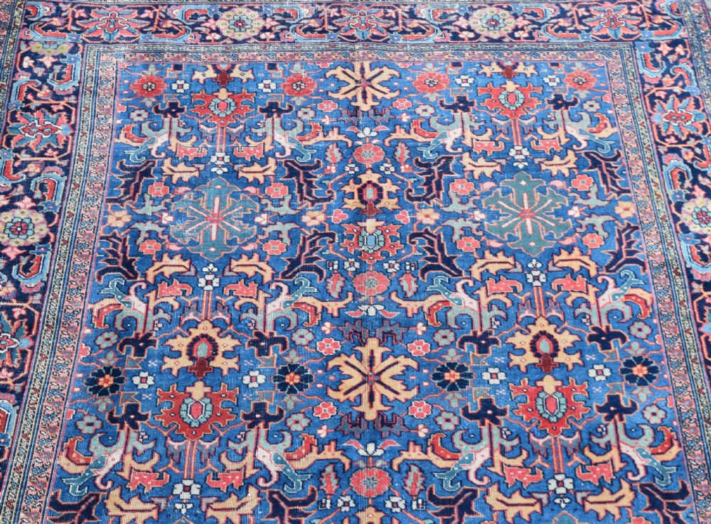 A hand-knotted wool carpet featuring an intricate blue central field covered in geometric floral motifs surrounded by a red and navy patterned border. View III