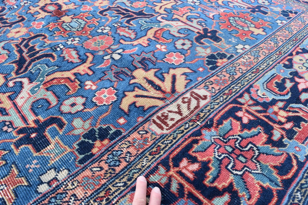 A hand-knotted wool carpet featuring an intricate blue central field covered in geometric floral motifs surrounded by a red and navy patterned border. View IV