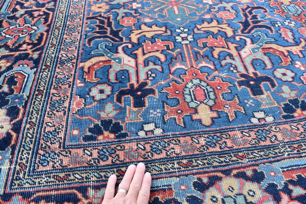 A hand-knotted wool carpet featuring an intricate blue central field covered in geometric floral motifs surrounded by a red and navy patterned border. View V