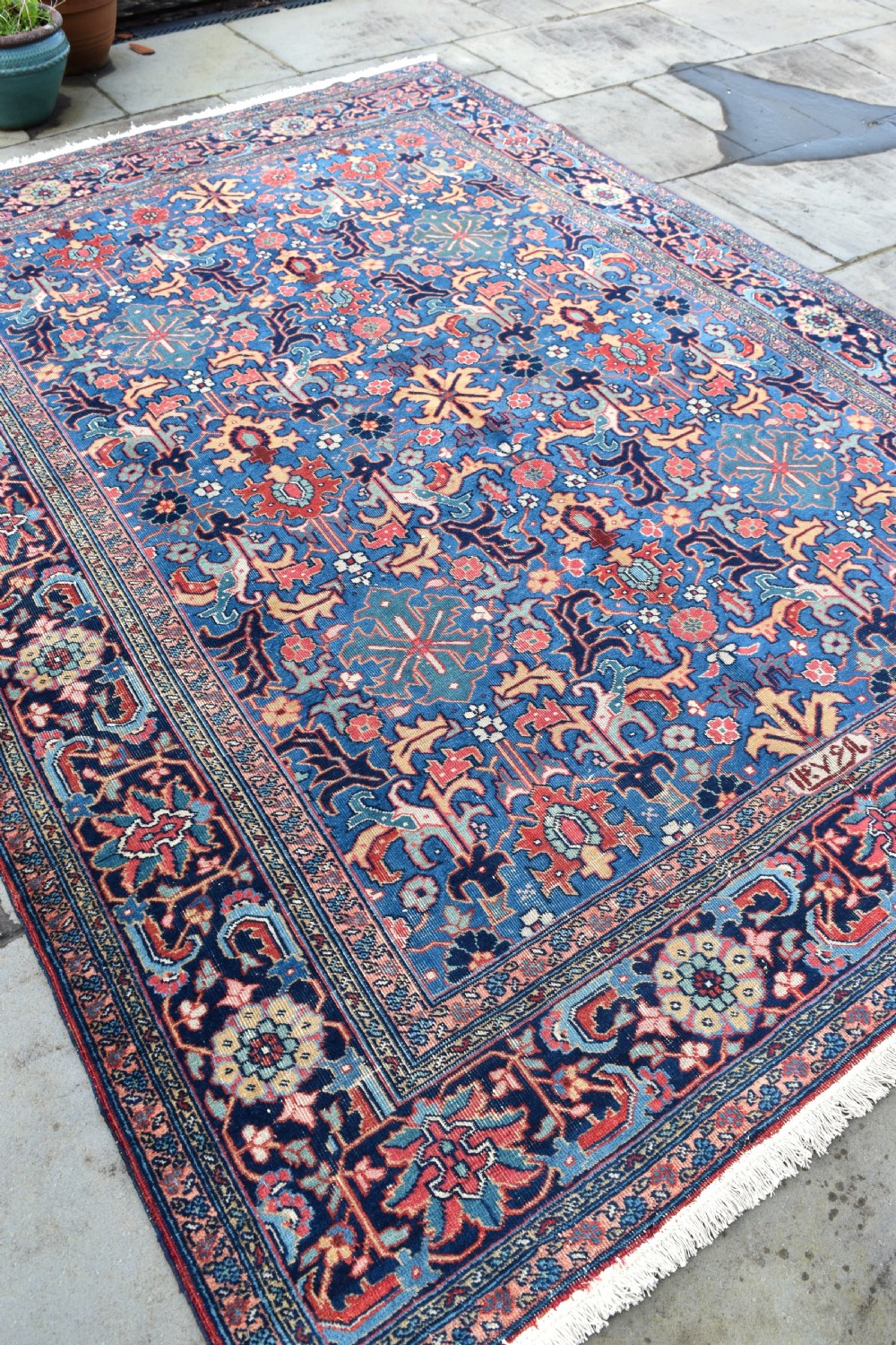A hand-knotted wool carpet featuring an intricate blue central field covered in geometric floral motifs surrounded by a red and navy patterned border. View VI