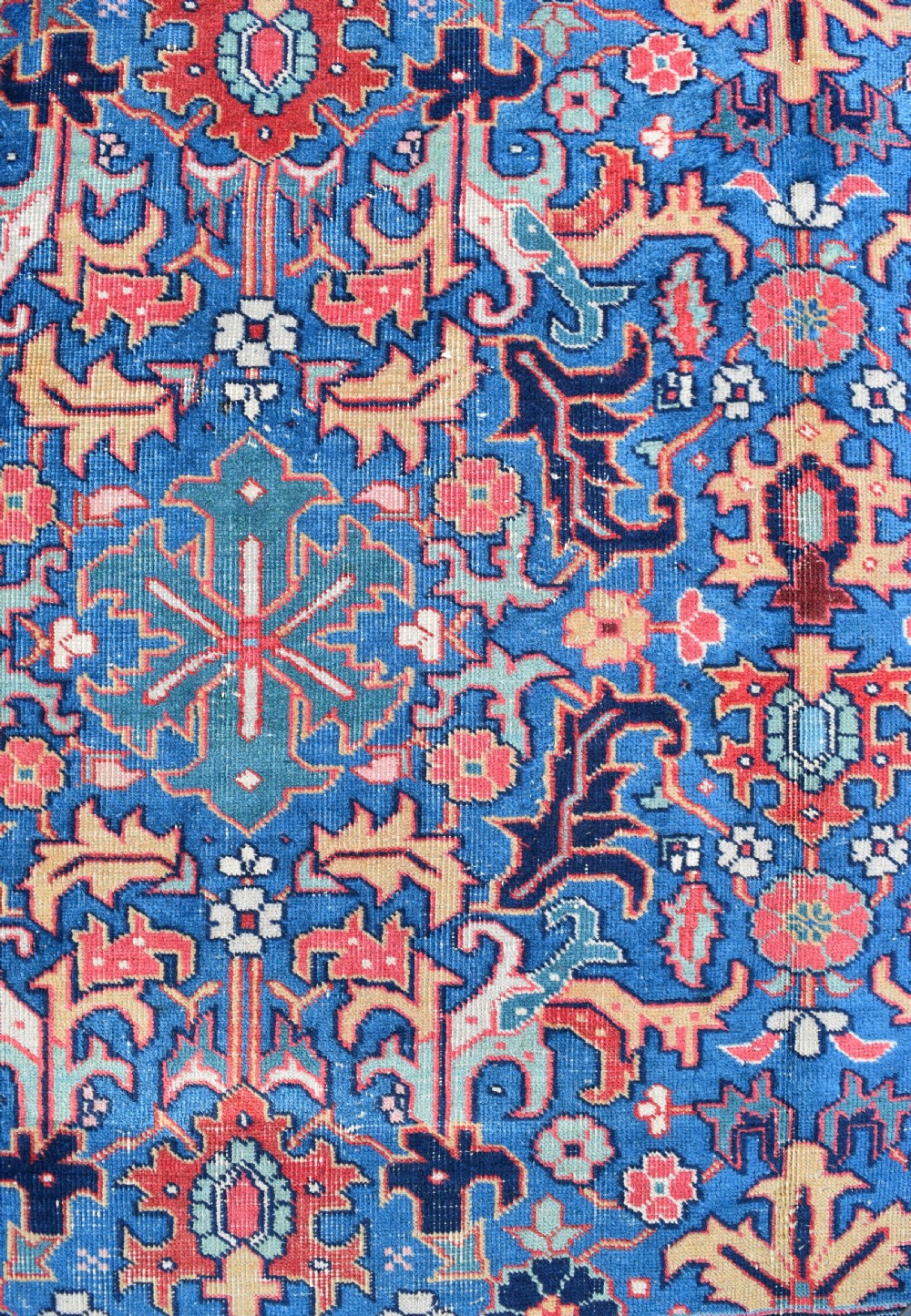 A hand-knotted wool carpet featuring an intricate blue central field covered in geometric floral motifs surrounded by a red and navy patterned border. View VII