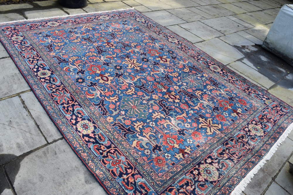 A hand-knotted wool carpet featuring an intricate blue central field covered in geometric floral motifs surrounded by a red and navy patterned border. View VIII