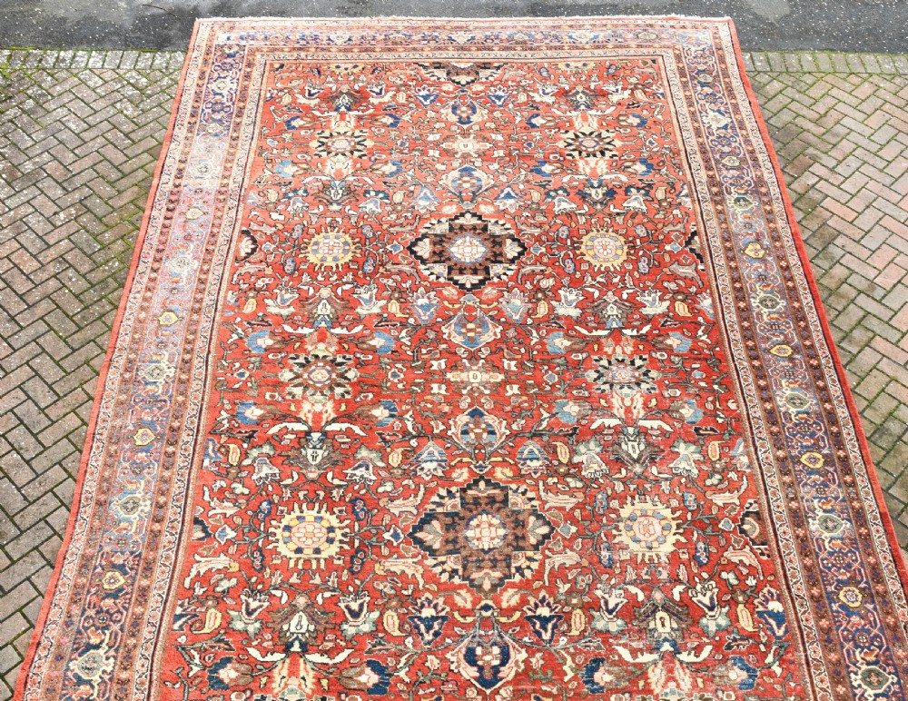 An oversized hand-knotted antique Persian Mahal carpet featuring an intricate terracotta red field and complex dark navy blue floral borders. View III