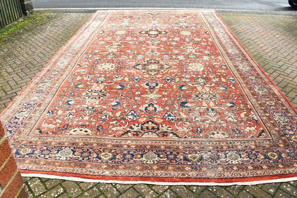 An oversized hand-knotted antique Persian Mahal carpet featuring an intricate terracotta red field and complex dark navy blue floral borders. View V