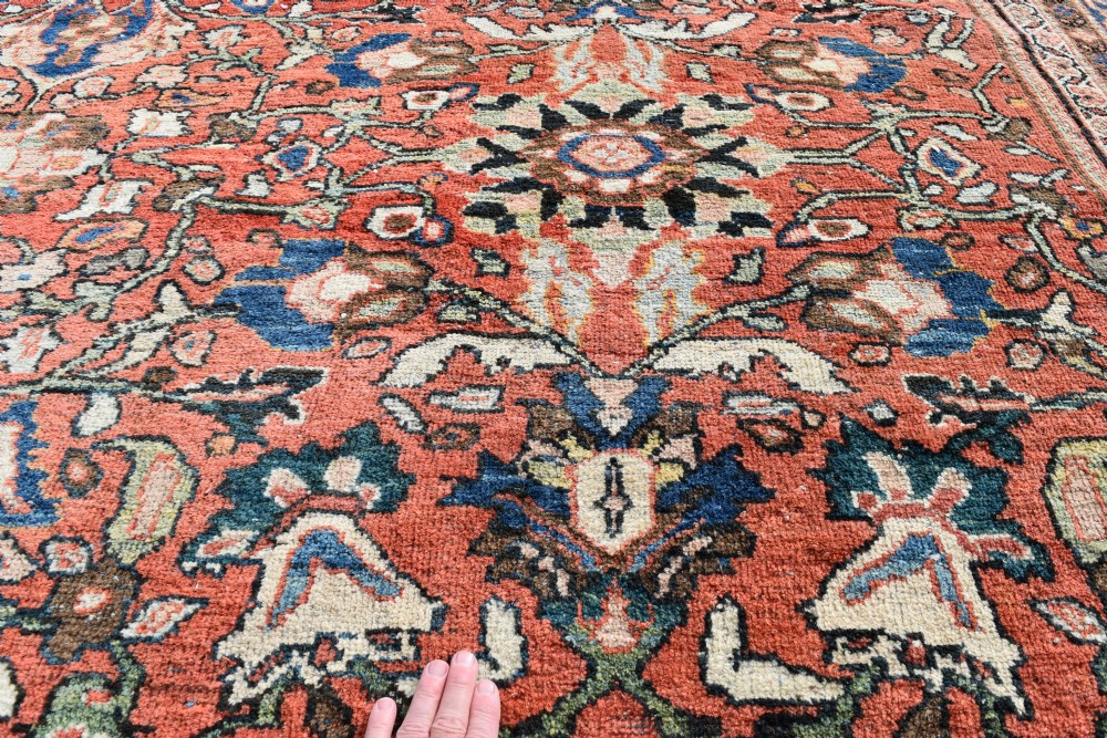 An oversized hand-knotted antique Persian Mahal carpet featuring an intricate terracotta red field and complex dark navy blue floral borders. View X