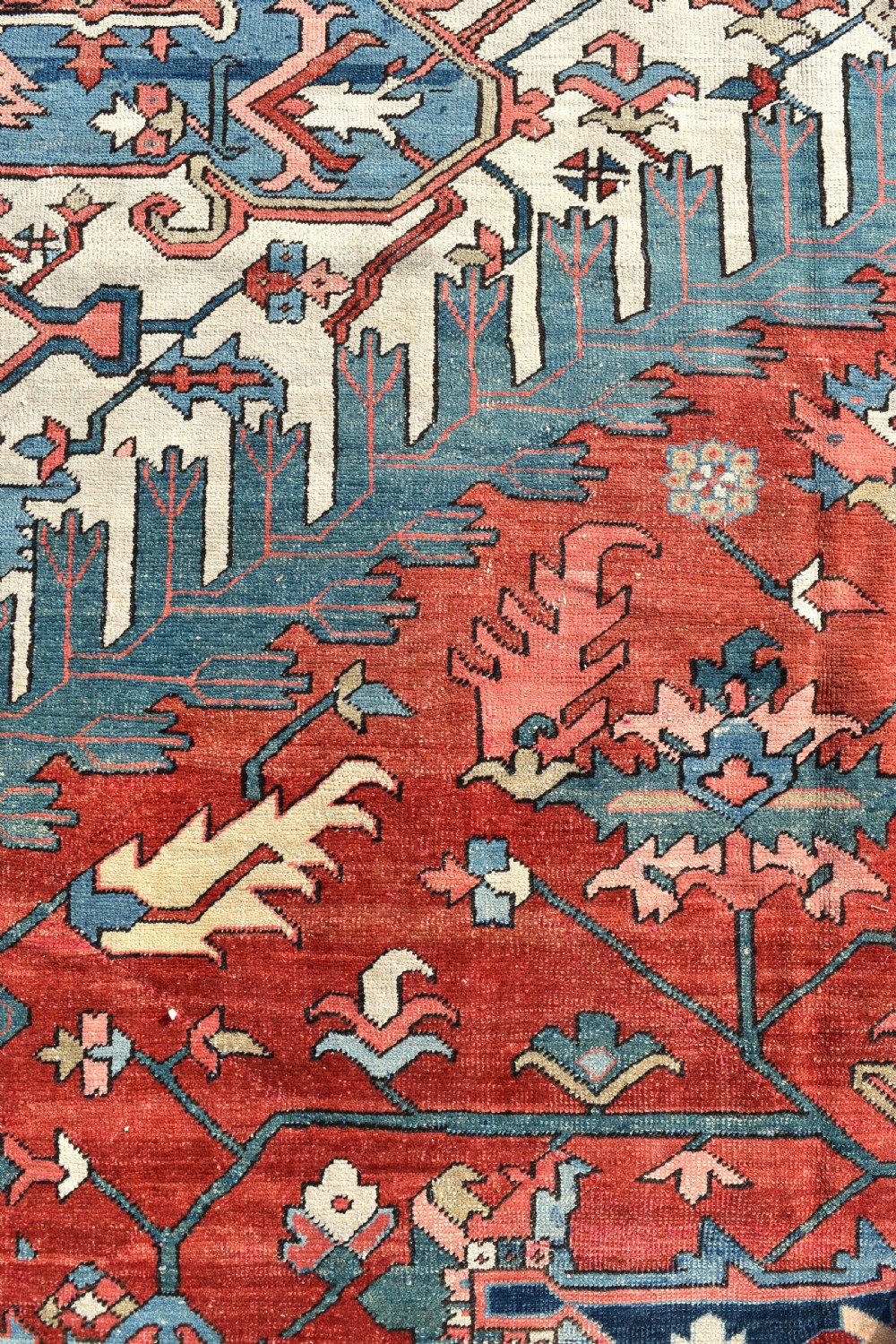 An oversize antique Heriz wool carpet featuring a prominent geometric central medallion in navy blue, beige, and red on a terracotta field with patterned spandrels and border. View VI