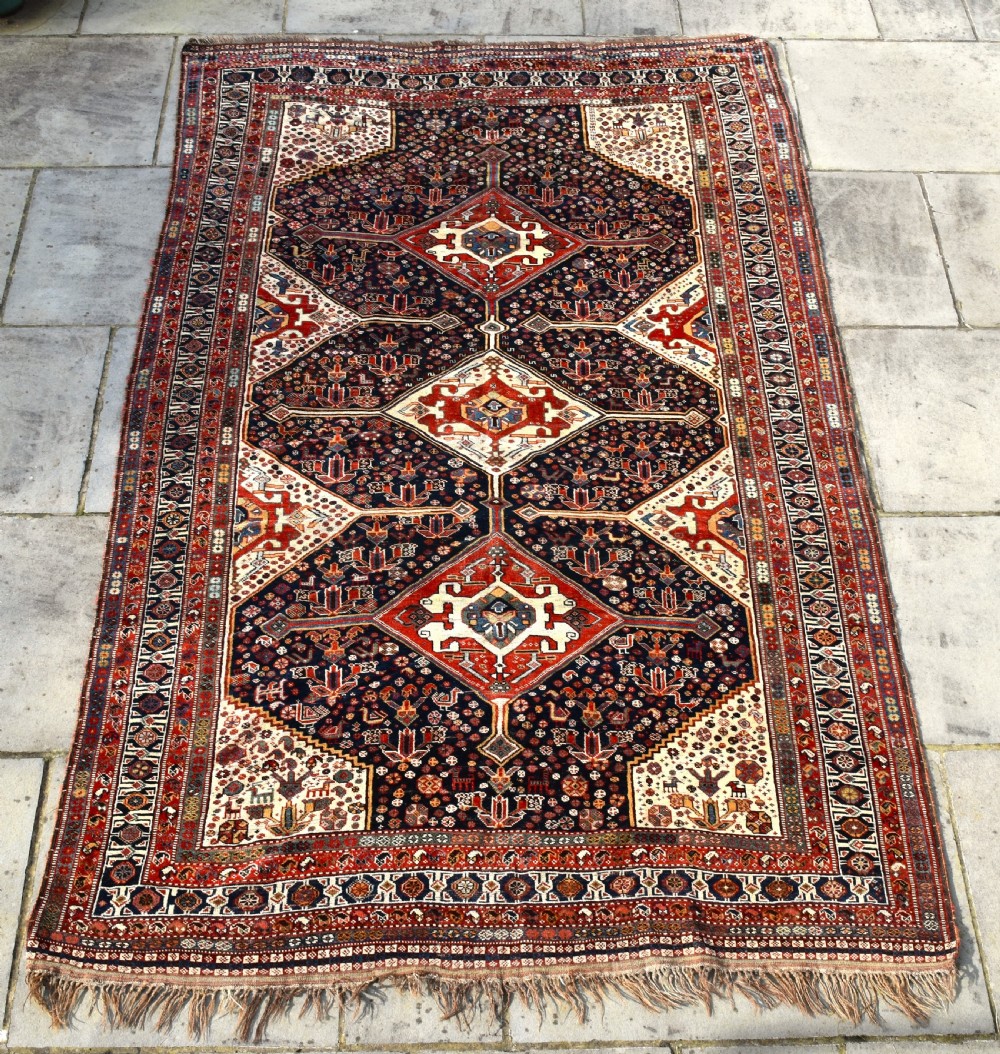 An antique hand-knotted Qashqai wool carpet featuring three central diamond medallions on a dark navy field surrounded by geometric borders.