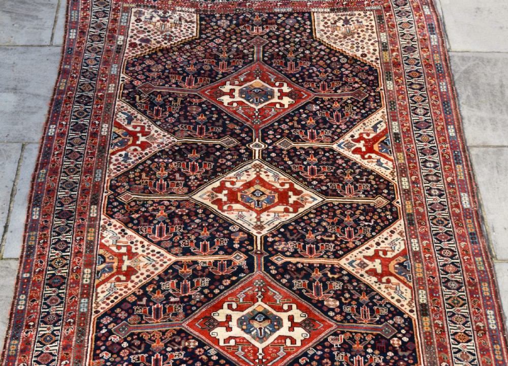 An antique hand-knotted Qashqai wool carpet featuring three central diamond medallions on a dark navy field surrounded by geometric borders. View III