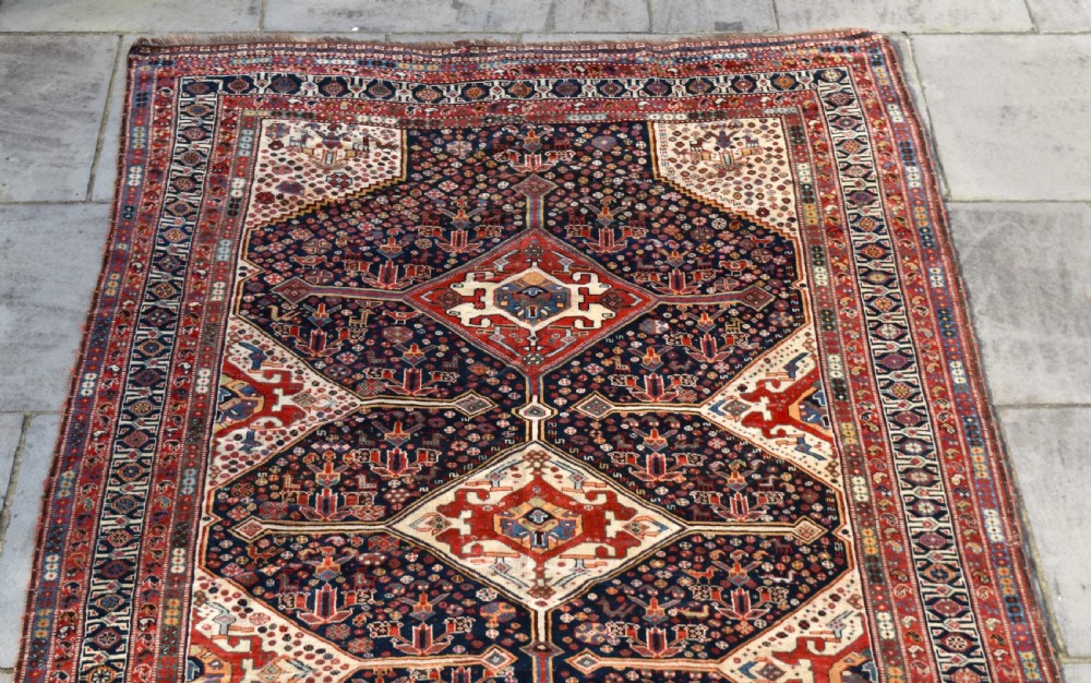 An antique hand-knotted Qashqai wool carpet featuring three central diamond medallions on a dark navy field surrounded by geometric borders. View IV