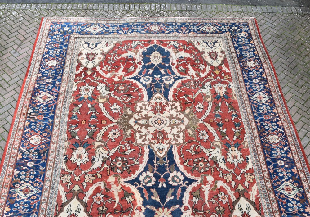 Large antique Ziegler Mahal wool carpet featuring a terracotta field with a central navy blue medallion and ornate floral borders. View V
