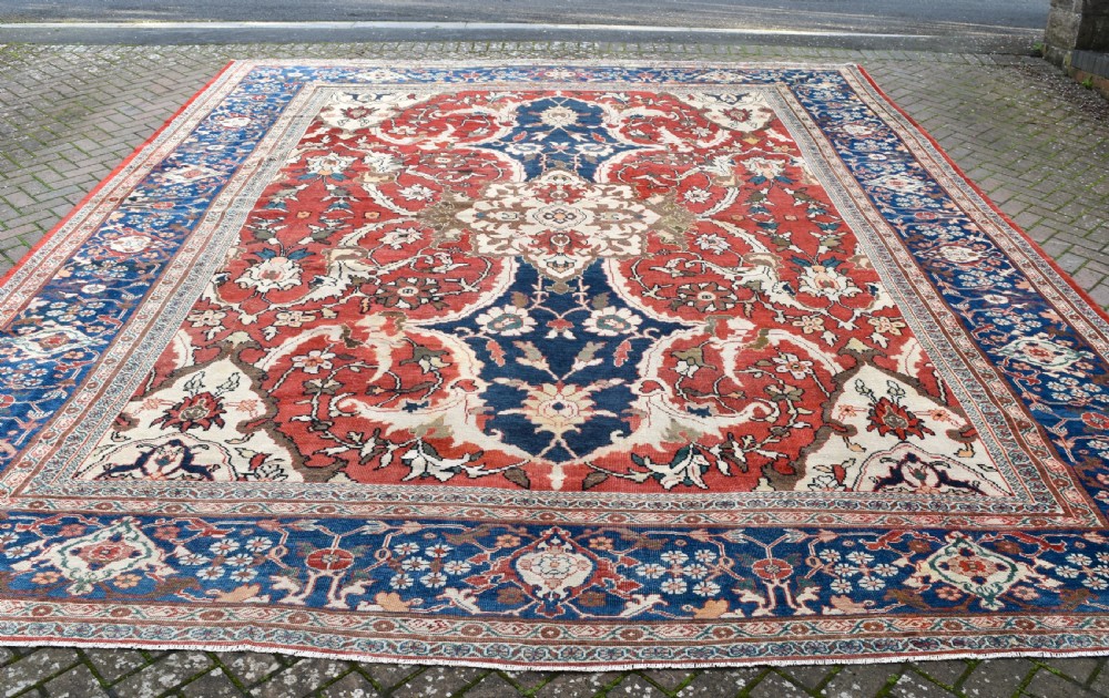 Large antique Ziegler Mahal wool carpet featuring a terracotta field with a central navy blue medallion and ornate floral borders. View VII