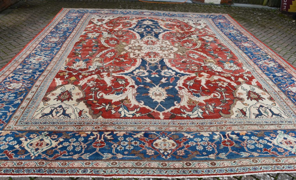 Large antique Ziegler Mahal wool carpet featuring a terracotta field with a central navy blue medallion and ornate floral borders. View XIII
