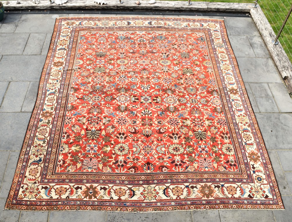 A large hand-knotted antique Persian Mahal carpet featuring a rust-red field filled with an intricate all-over floral pattern surrounded by a contrasting cream main border.