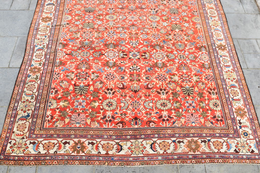 A large hand-knotted antique Persian Mahal carpet featuring a rust-red field filled with an intricate all-over floral pattern surrounded by a contrasting cream main border. View II