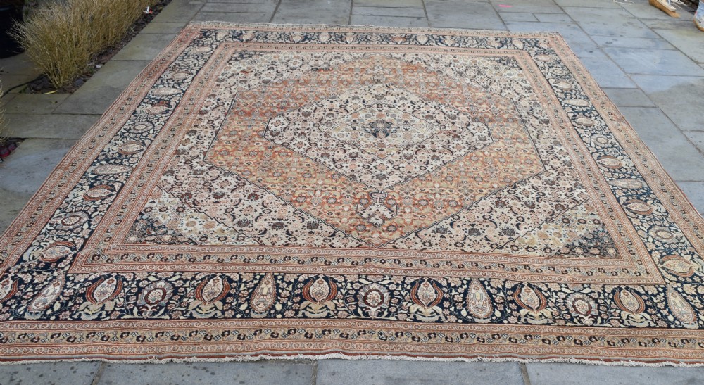 A large antique hand-knotted Tabriz carpet featuring an intricate central medallion in terracotta and cream framed by a wide navy floral border.