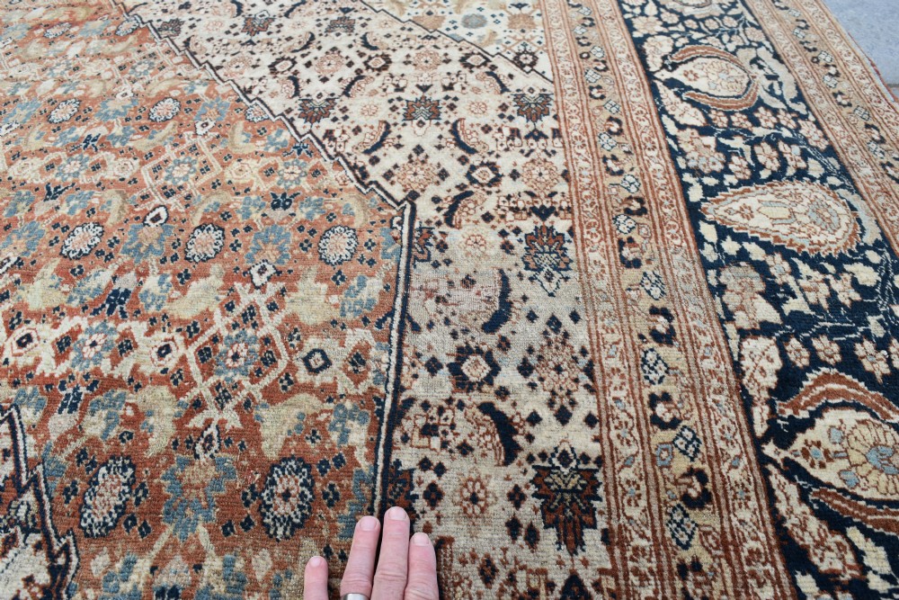 A large antique hand-knotted Tabriz carpet featuring an intricate central medallion in terracotta and cream framed by a wide navy floral border. View II