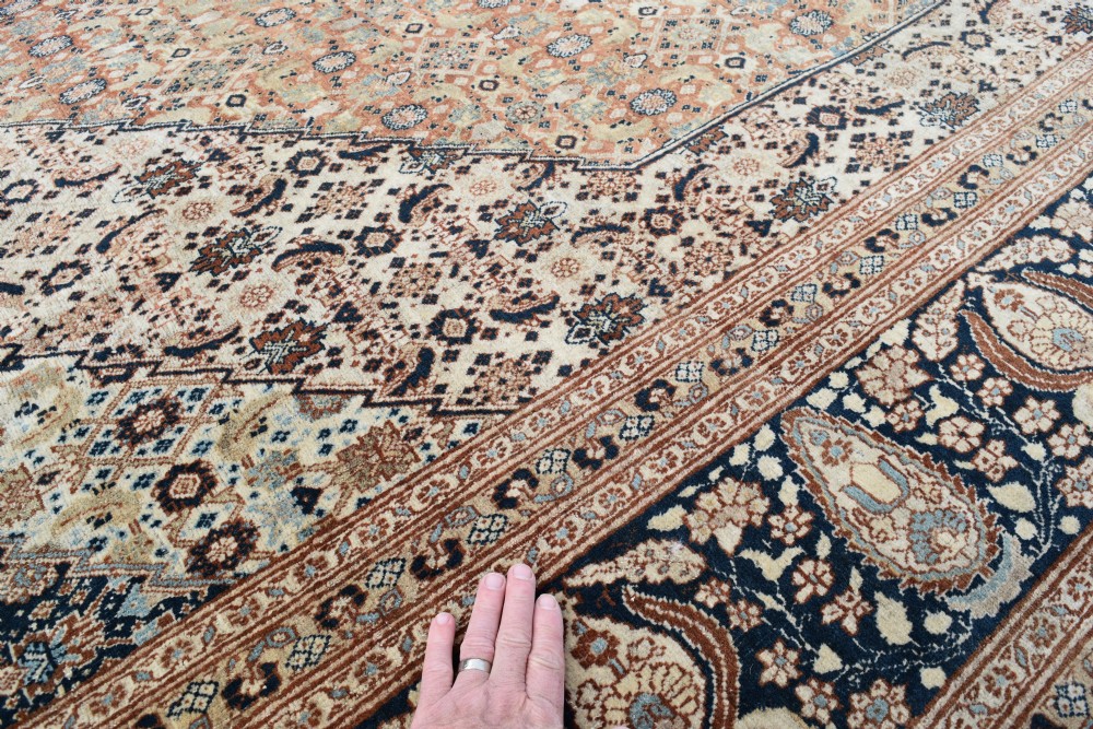 A large antique hand-knotted Tabriz carpet featuring an intricate central medallion in terracotta and cream framed by a wide navy floral border. View III