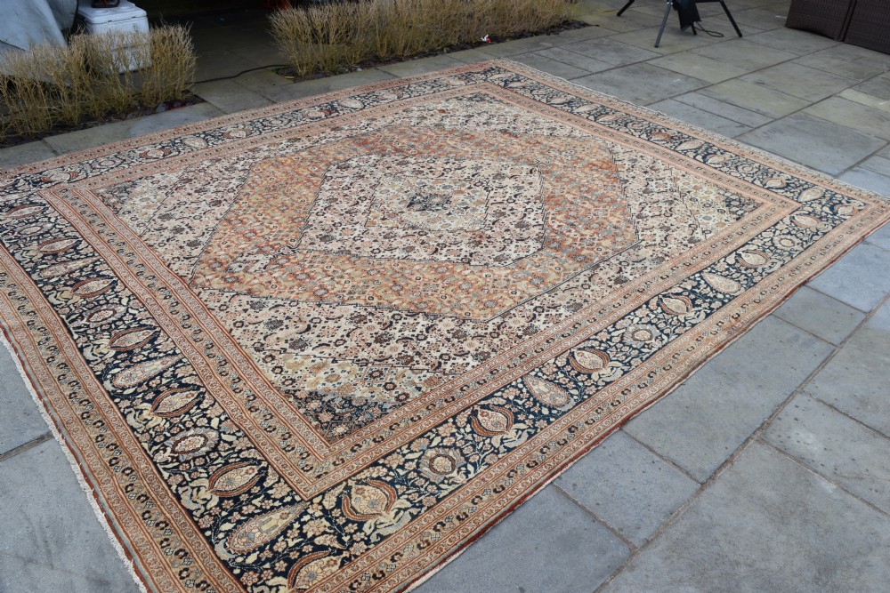 A large antique hand-knotted Tabriz carpet featuring an intricate central medallion in terracotta and cream framed by a wide navy floral border. View V