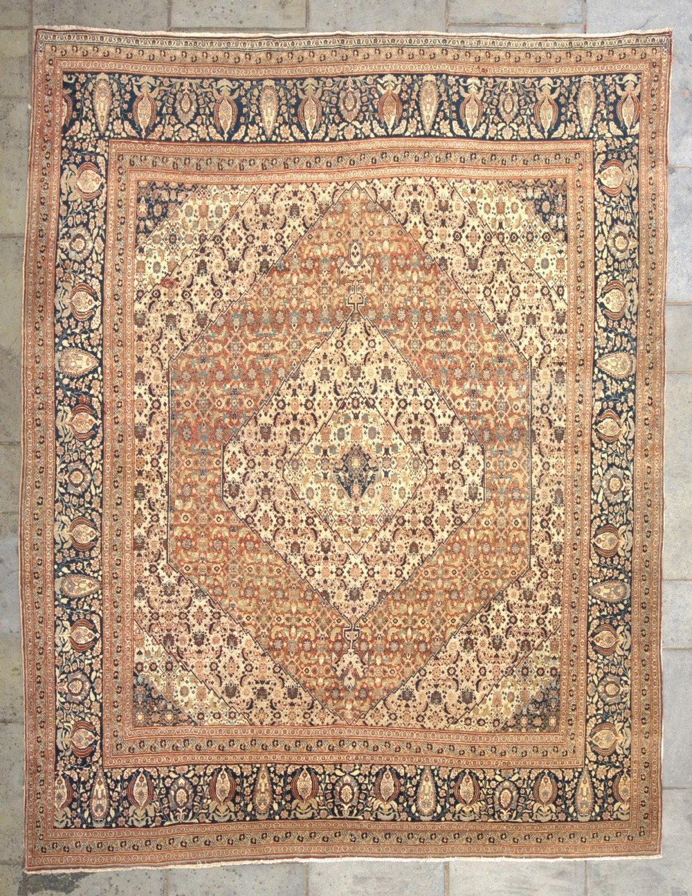 A large antique hand-knotted Tabriz carpet featuring an intricate central medallion in terracotta and cream framed by a wide navy floral border. View VI