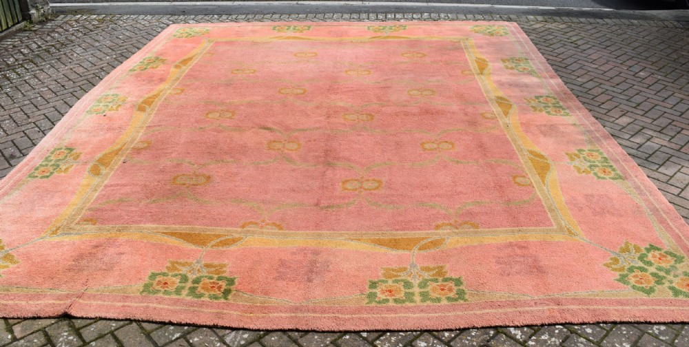A large Arts and Crafts hand-knotted wool carpet in pink featuring mustard yellow and green stylised floral borders.