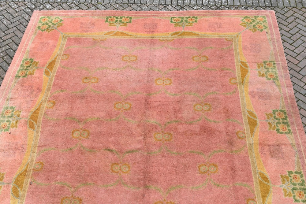 A large Arts and Crafts hand-knotted wool carpet in pink featuring mustard yellow and green stylised floral borders. View IV