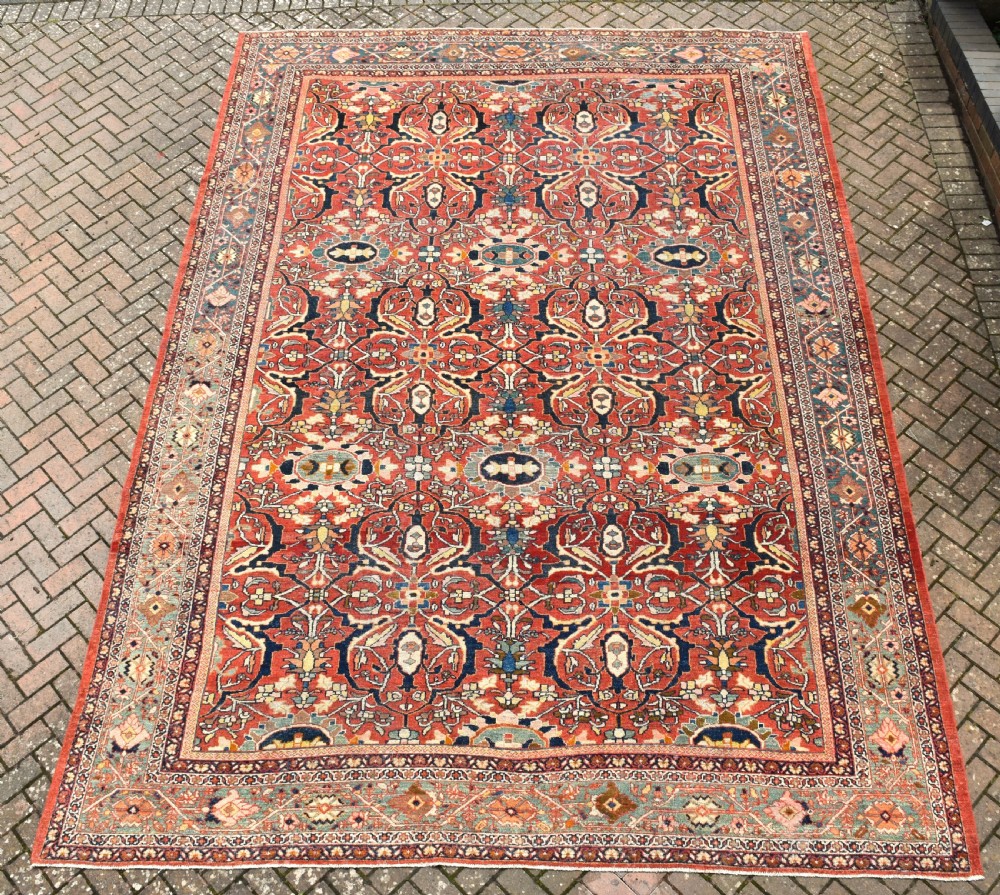 A large rectangular hand-knotted Persian Mahal carpet featuring a terracotta red ground with an all-over navy blue and beige floral palmette pattern framed by intricate borders.