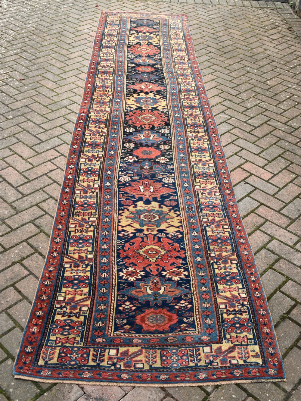 A long hand-knotted wool runner rug featuring repeating geometric medallions in red, navy blue, and yellow along framed patterned borders. View II