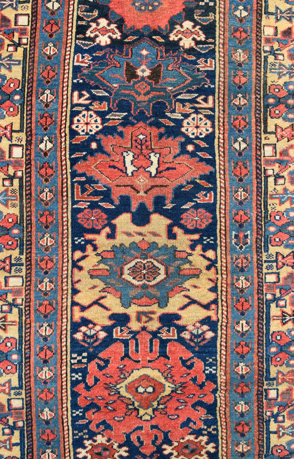 A long hand-knotted wool runner rug featuring repeating geometric medallions in red, navy blue, and yellow along framed patterned borders. View III