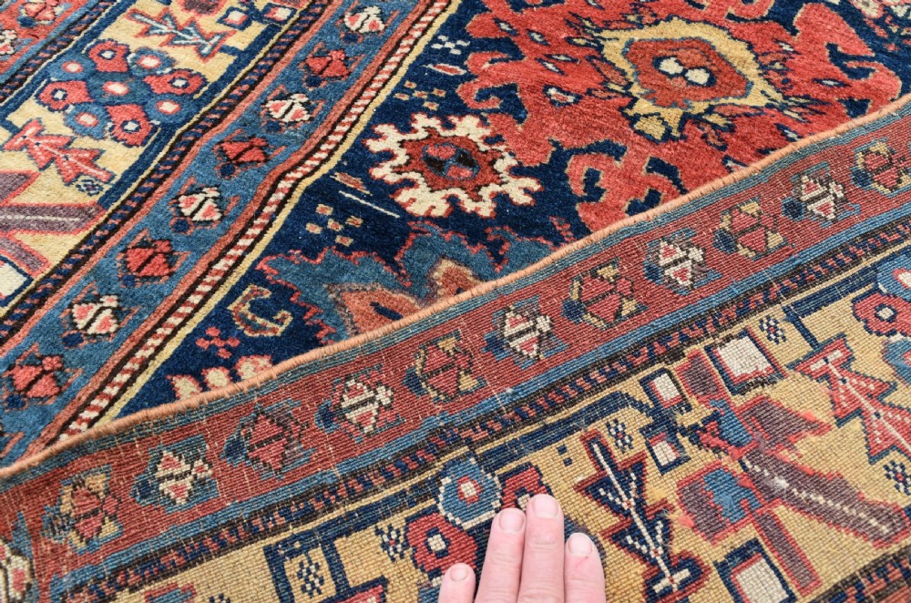 A long hand-knotted wool runner rug featuring repeating geometric medallions in red, navy blue, and yellow along framed patterned borders. View VII