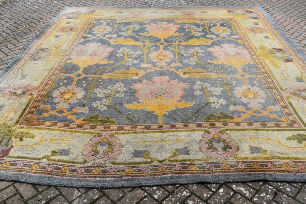 A large hand-knotted Gavin Morton Donegal wool carpet featuring stylised floral motifs in pink, ochre, and green across a slate blue field.