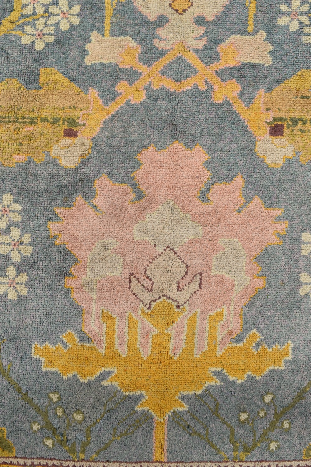 A large hand-knotted Gavin Morton Donegal wool carpet featuring stylised floral motifs in pink, ochre, and green across a slate blue field. View V