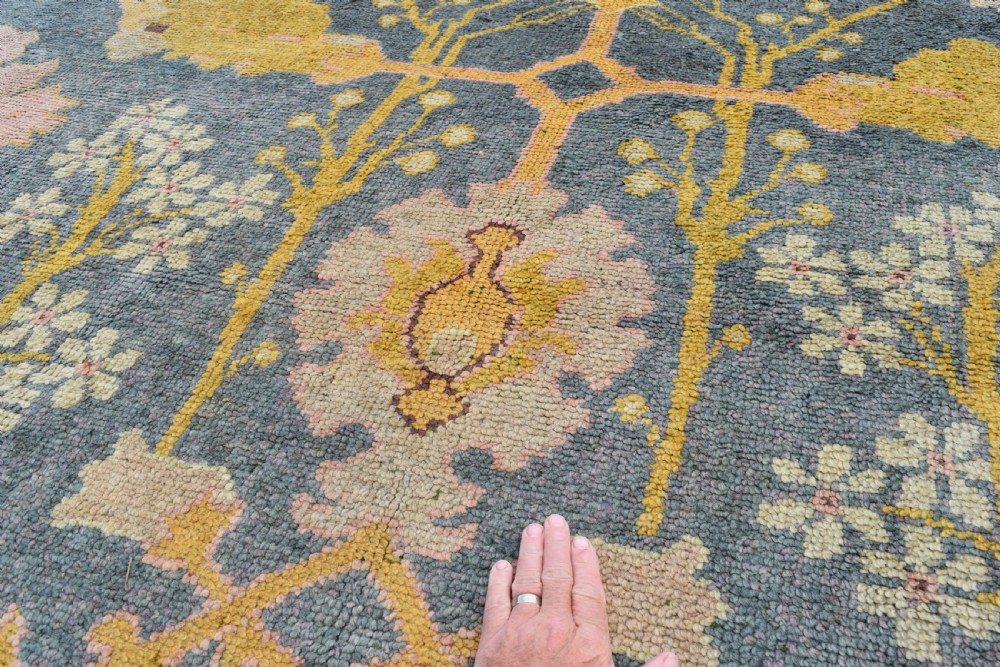 A large hand-knotted Gavin Morton Donegal wool carpet featuring stylised floral motifs in pink, ochre, and green across a slate blue field. View VI