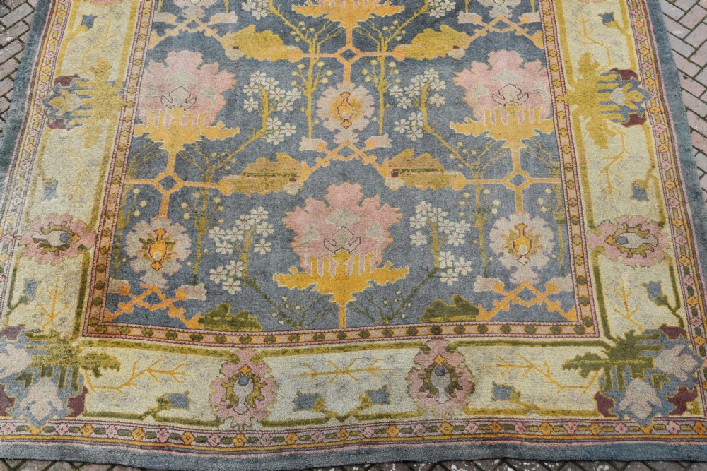 A large hand-knotted Gavin Morton Donegal wool carpet featuring stylised floral motifs in pink, ochre, and green across a slate blue field. View VIII