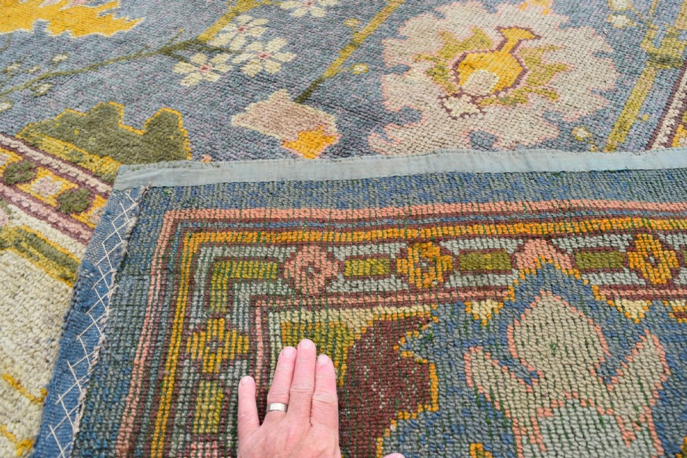 A large hand-knotted Gavin Morton Donegal wool carpet featuring stylised floral motifs in pink, ochre, and green across a slate blue field. View IX